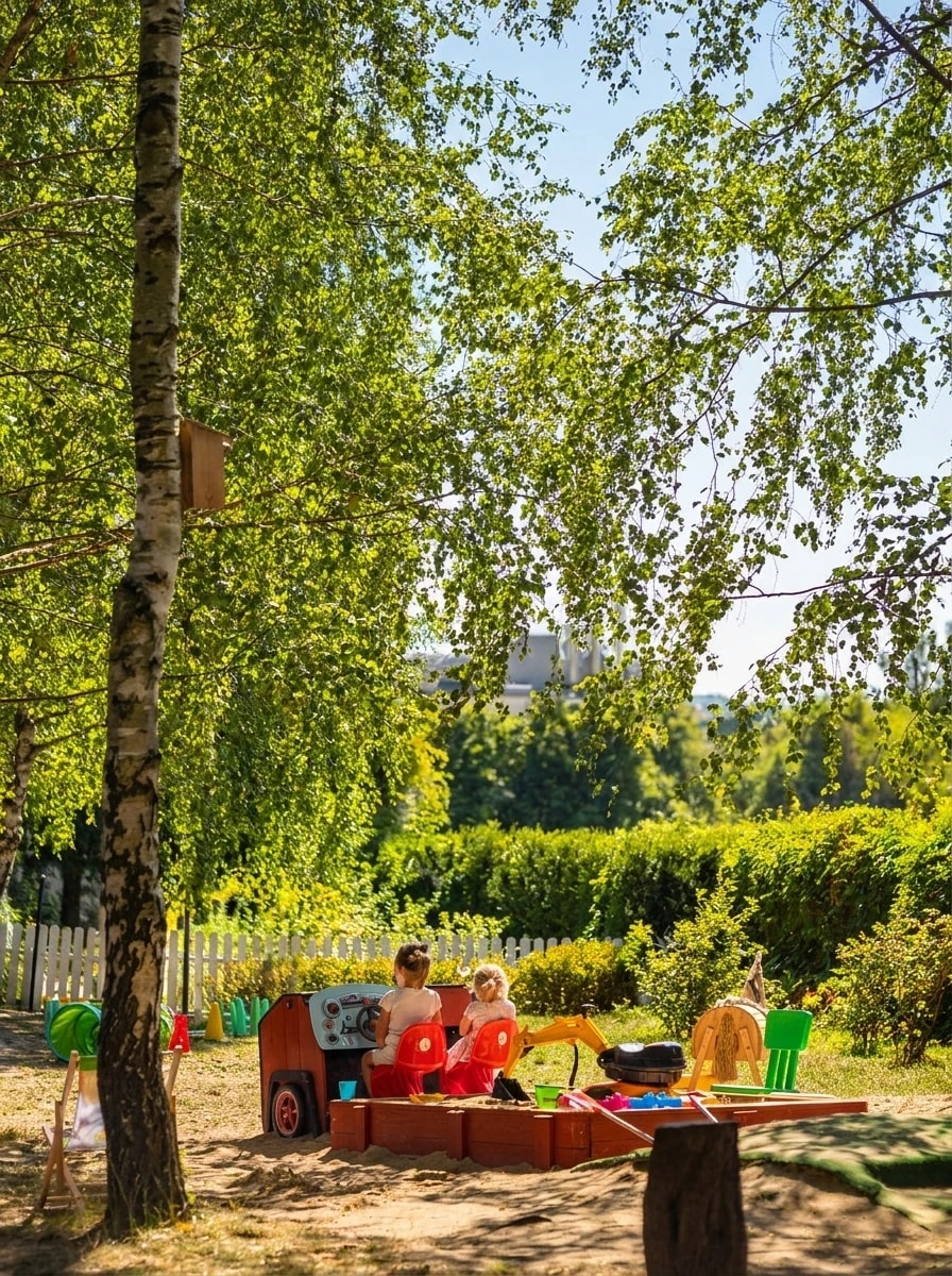 Dwie dziewczynki bawiące się w piaskownicy w słonecznym, zadrzewionym ogrodzie przedszkola Zaczarowany Ogród